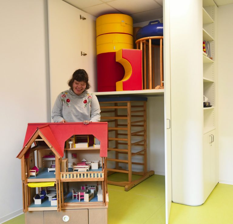 Marie holt das große Puppenhaus aus dem maßgefertigten Spieleschrank, der jetzt in den Räumen der Frühförderung der Lebenshilfe in Marxheim eingebaut wurde. Die weiche Rundung des Möbelstücks senkt die Verletzungsgefahr, wenn die kleinen Kinder mal umhertoben. Foto: Knapp