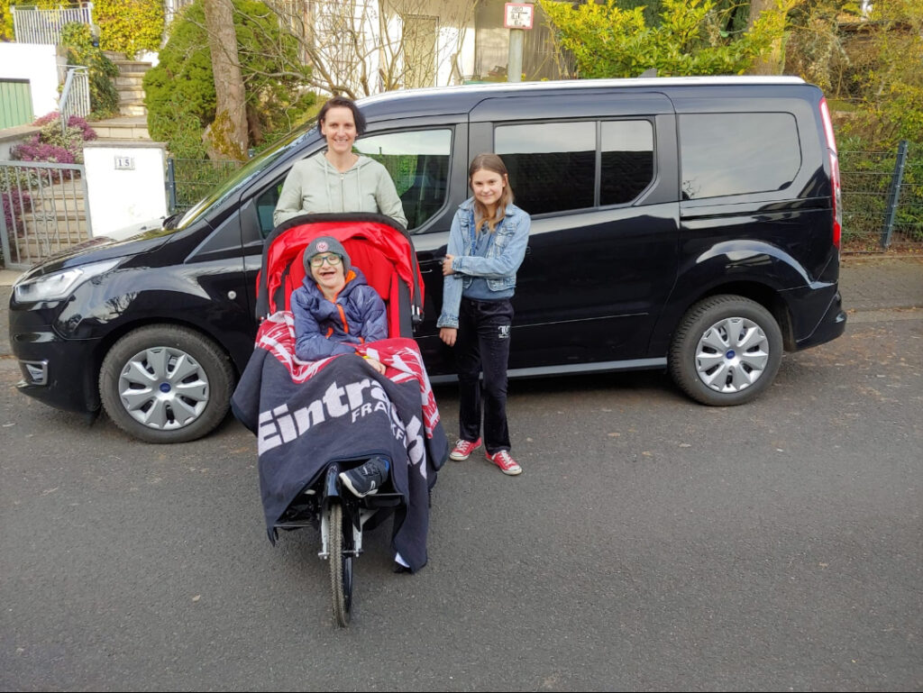 Nicole Steinmann steht mit ihrer Tochter vor dem neuen Fahrzeug. Ihr Sohn ist in eine Eintracht-Decke gehüllt. Foto: Privat